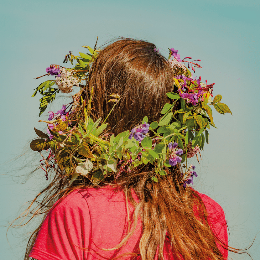 Visuel de la fête de la Saint-Jean et du solstice d'été avec une femme de dos, cheveux longs lâchés et une couronne de fleurs violettes sur la tête