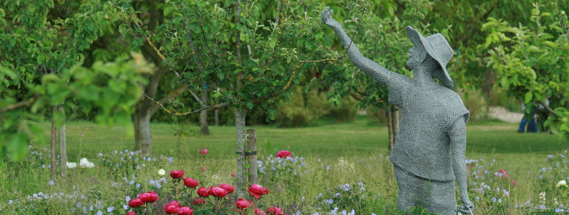 œuvre d'art en grillage à poule représentant un humain portant un panier qui cueille quelque chose dans un arbre dans le verger prairie