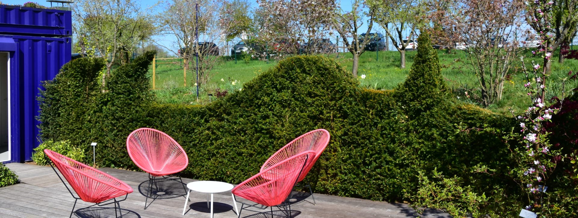 Haie de taxus taillée en vague sur en bordure de terrasse avec un salon de jardin Acapulco orange en premier plan