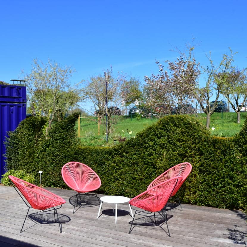 Haie de taxus taillée en vague sur en bordure de terrasse avec un salon de jardin Acapulco orange en premier plan