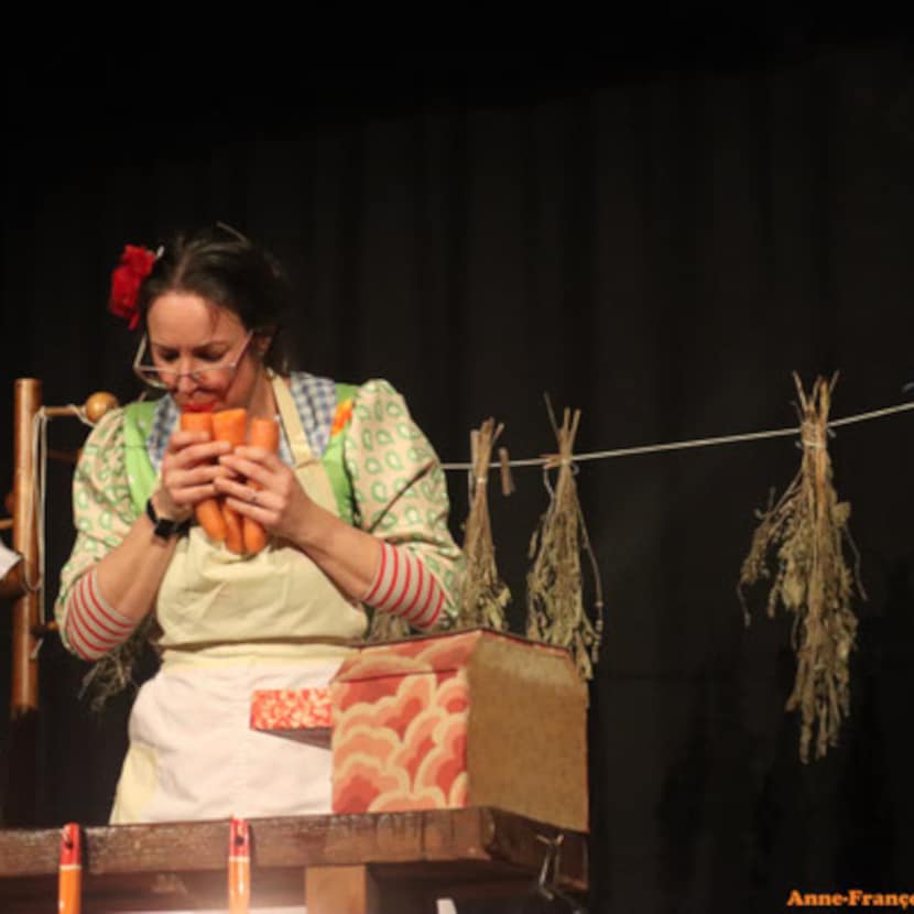 Comédienne qui souffle dans une flûte de pan réalisée avec des carottes, dans un décor de cuisine.