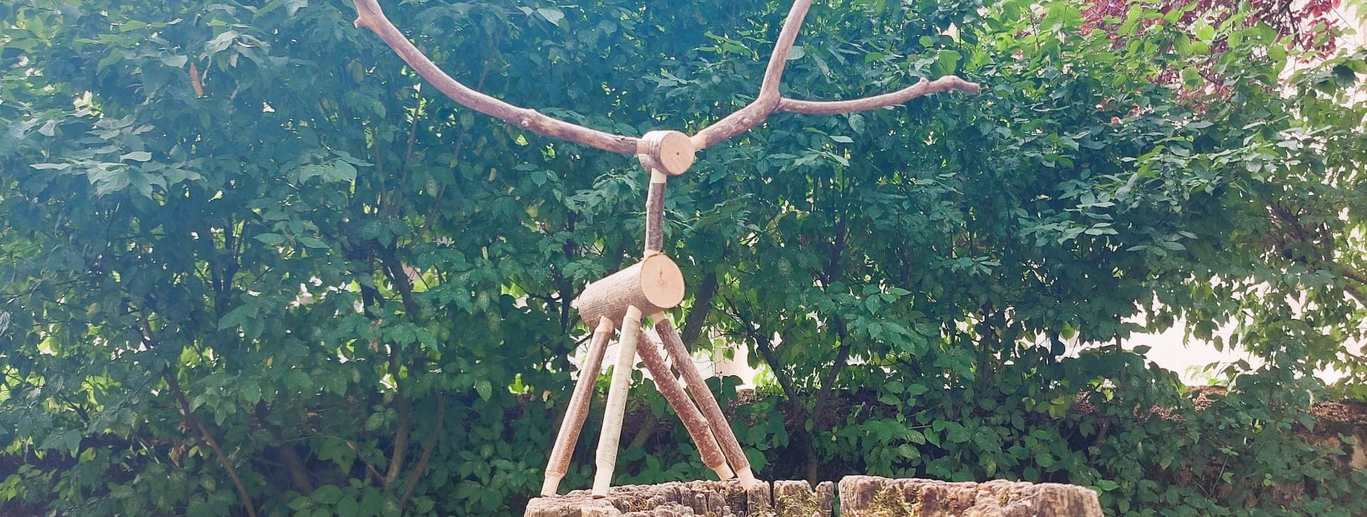 Animal figurant un cerf fabriqué à partir de rondins et de banches, au second plan, des arbres.