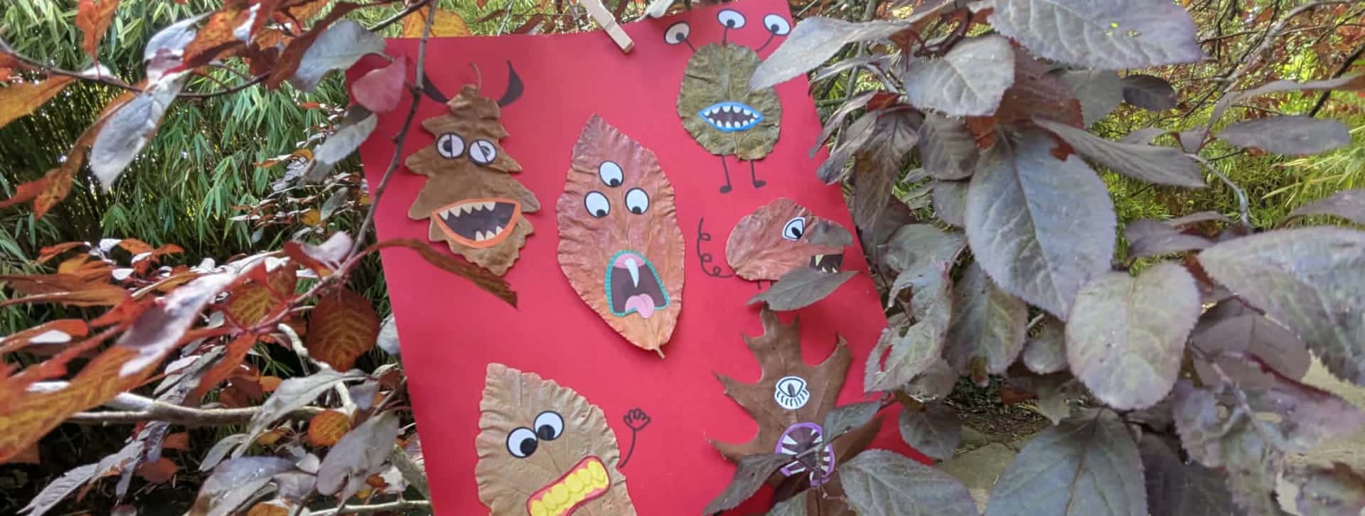 6 monstres grimaçants fabriqués à partir de feuilles mortes, collés sur une feuille rouge, elle même posée au milieu de feuille de charmille bronze.