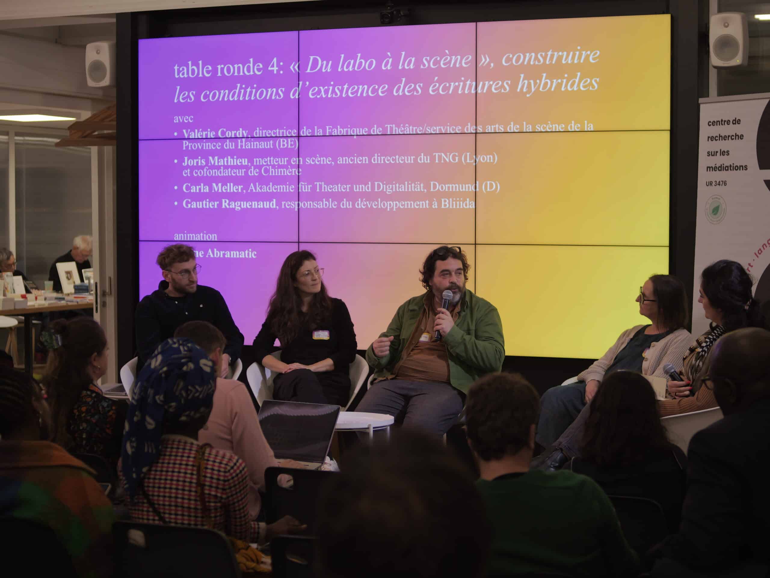 Plusieurs personnes assises autour d'une table ronde échangent. Au fond un écran avec la thématique de la discussion